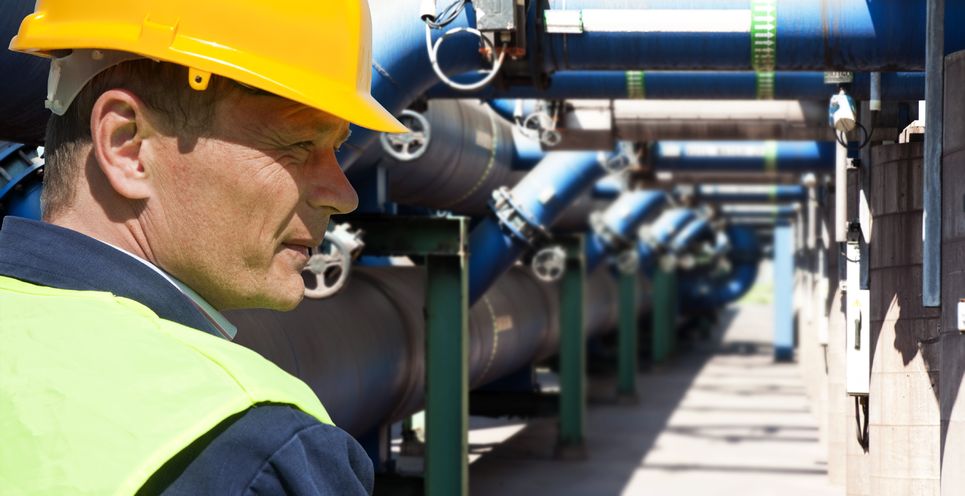 Werknemer met helm bij industriele leidingen